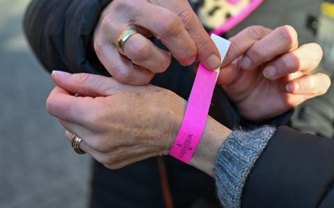 Frau bekommt ein Bändchen zum Einkaufen ums Handgelenk gelegt.