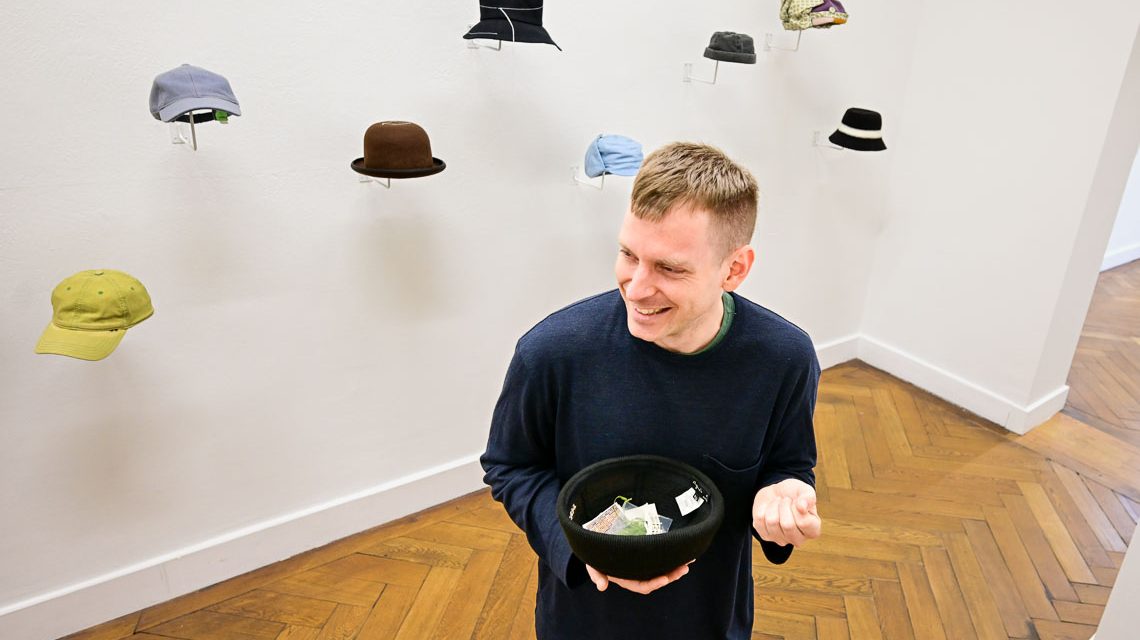 Martin La Roche und sein Musée Legitime, er nimmt die Kopfbedeckung ab und stellt die Ausstellungsstücke vor.