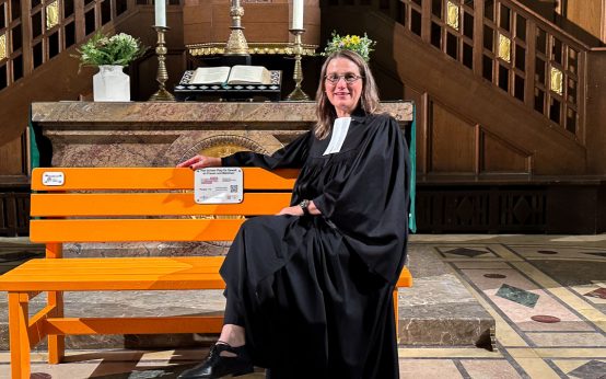 Für die Predigt hat Pfarrerin Ursula Kuhn die orangefarbene Bank vor den Altar gestellt: „Diese Bank schreit uns förmlich an: Schaut hin! Sprecht darüber! Nehmt die Geschichten ernst! Schweigen ist keine Option“, sagt sie im Gottesdienst.